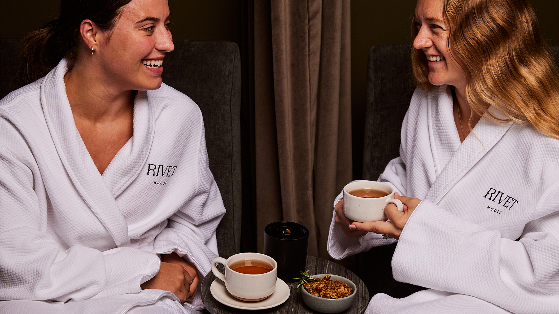 two women in bathrobes sitting at a table with cups of tea