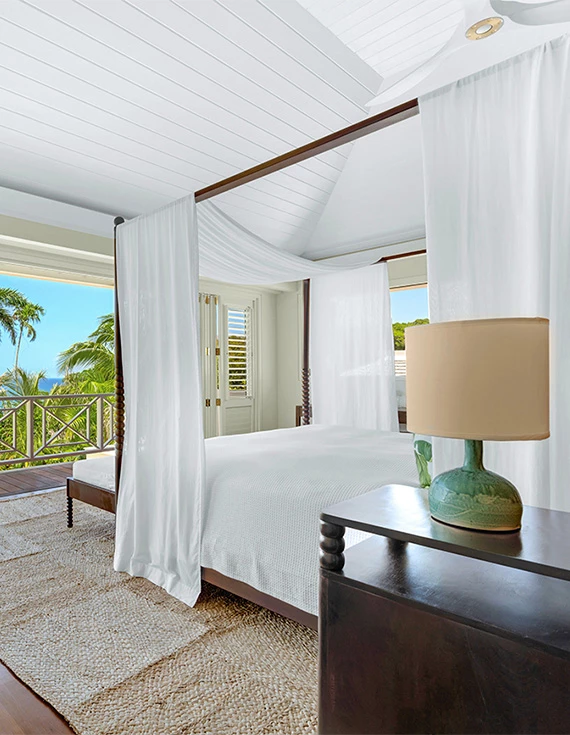 a bed with white curtains and a lamp on a table