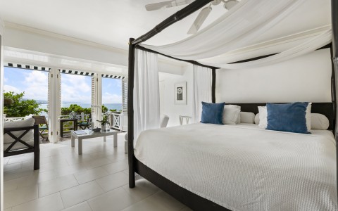 a bed with white sheets and blue pillows in a room with a balcony and ocean