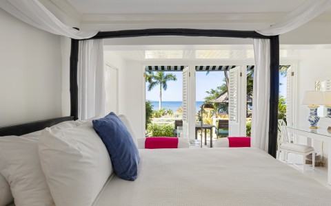 a bed with white sheets and blue pillows in a room with a beach view
