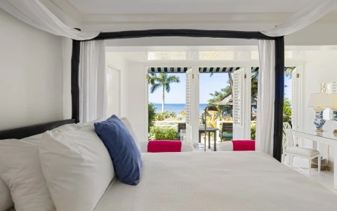 a bed with white sheets and blue pillows in a room with a beach view