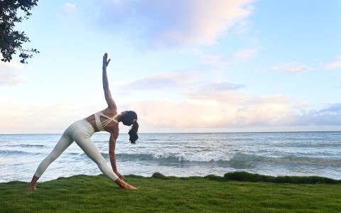 a woman stretching on grass by the ocean