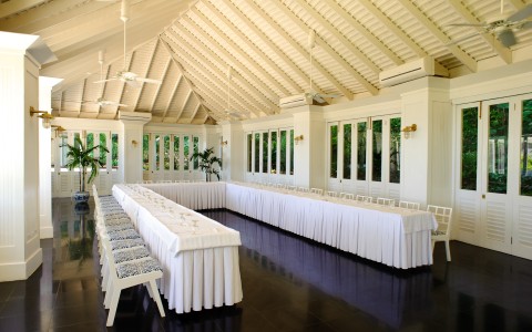a long white table with white tablecloths and chairs in a room with windows