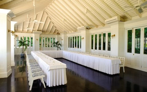 a long white table with white tablecloths and chairs in a room with windows