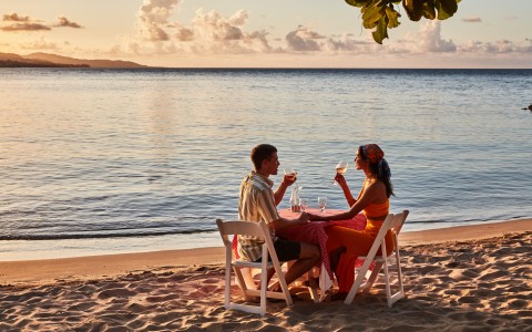 a man and woman sitting at a table on a beach