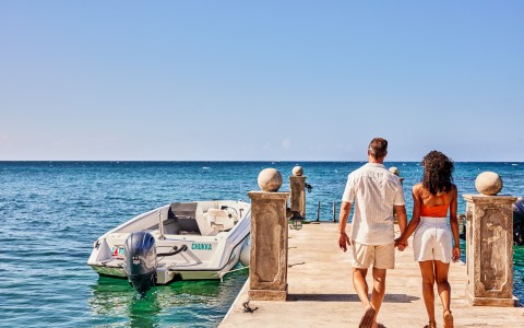a man and woman holding hands walking on a dock with a boat in the water