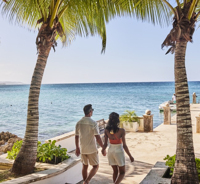 a man and woman holding hands walking on a beach