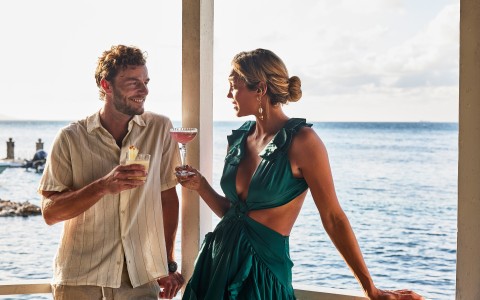 a man and woman standing on a balcony by the ocean