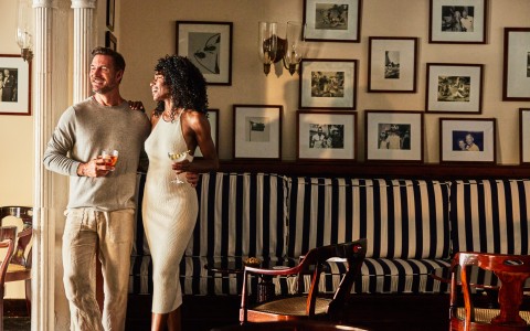 a man and woman standing in a room with a couch and pictures on the wall