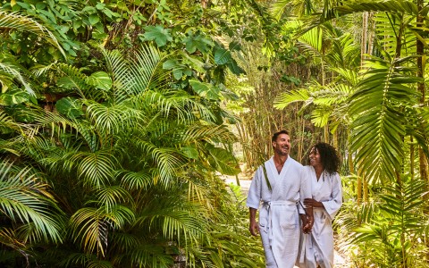 a man and woman in white robes walking on a path surrounded by trees