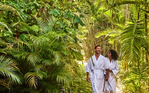 a man and woman in white robes walking on a path surrounded by trees