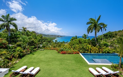 a pool and chairs in a garden with a body of water in the background