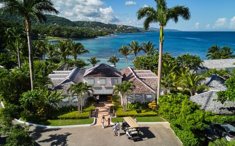 a group of people walking in front of a house with palm trees and a body of water