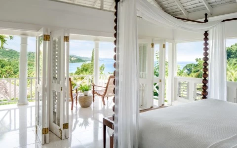 a bedroom with a canopy bed and a chair and a view of the ocean