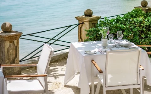 a table set up with a white tablecloth and chairs on a patio overlooking water