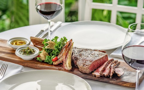 a steak on a wooden board next to a glass of wine