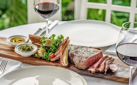 a steak on a wooden board next to a glass of wine