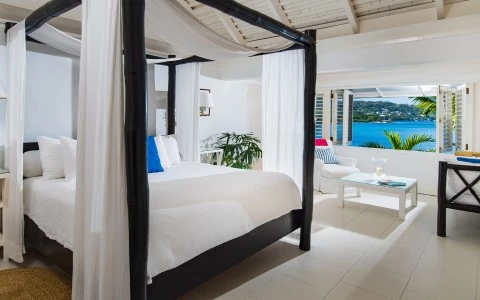 a bed with white curtains and a table in front of a large body of water