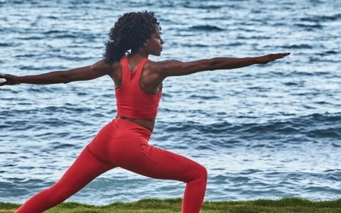 a woman in red yoga outfit stretching out in front of water