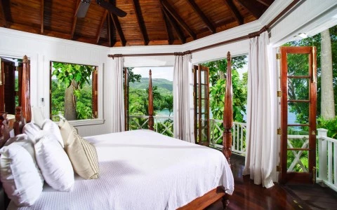 a room with a bed and a balcony with trees and a view of the ocean