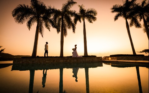 a man and woman standing next to a pool with palm trees