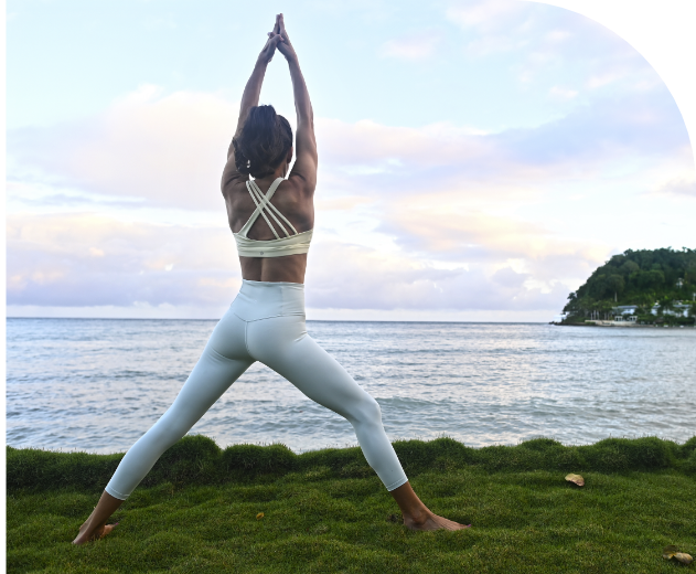 a woman in white yoga outfit standing on grass by water