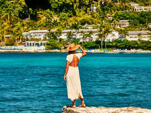 a woman in a white dress and hat standing on a rock by the water