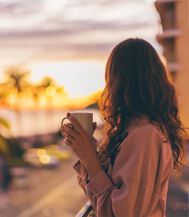 a woman holding a cup looking out a window