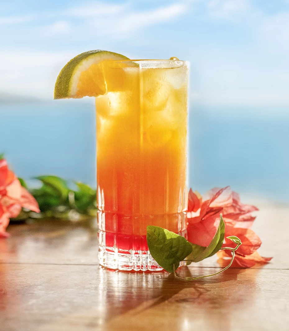 a glass of orange and yellow drink with a slice of lime on top of it