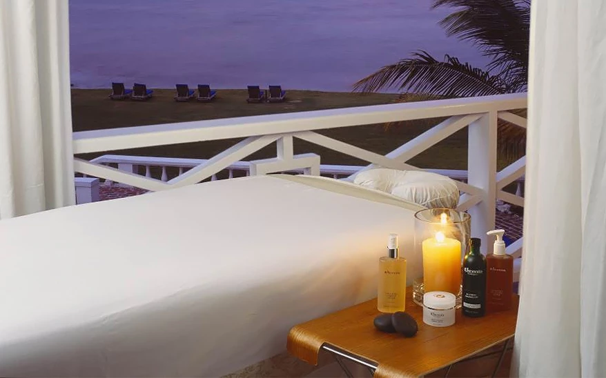 a bed with a candle and a table on a balcony overlooking the ocean