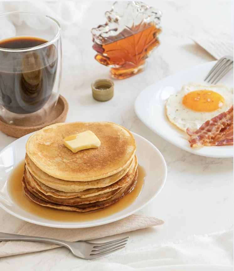 a stack of pancakes with butter and bacon on a plate next to a cup of coffee