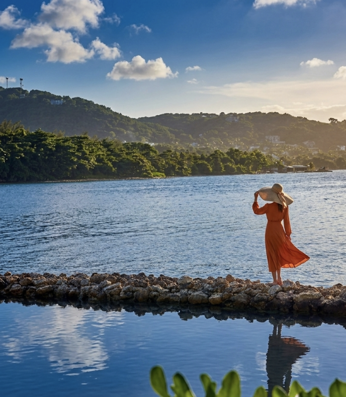 a woman in a red dress and hat standing on rocks by water