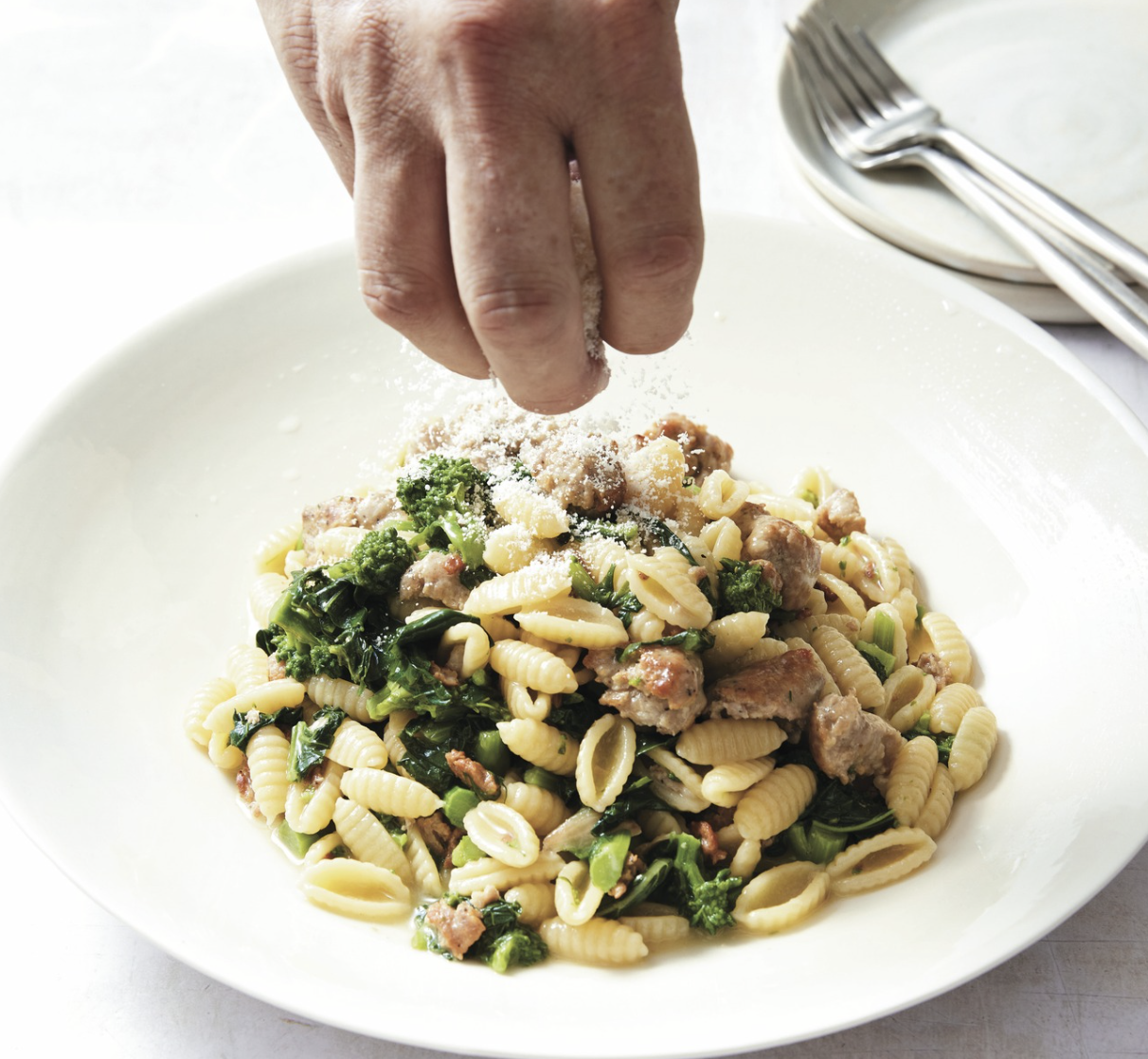 a hand sprinkling cheese over pasta