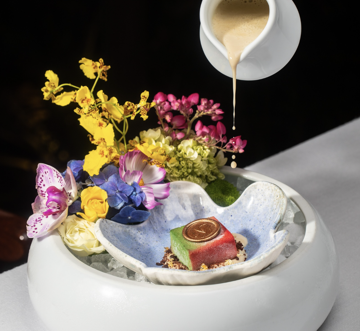 a bowl of food with flowers and a pitcher pouring liquid into it