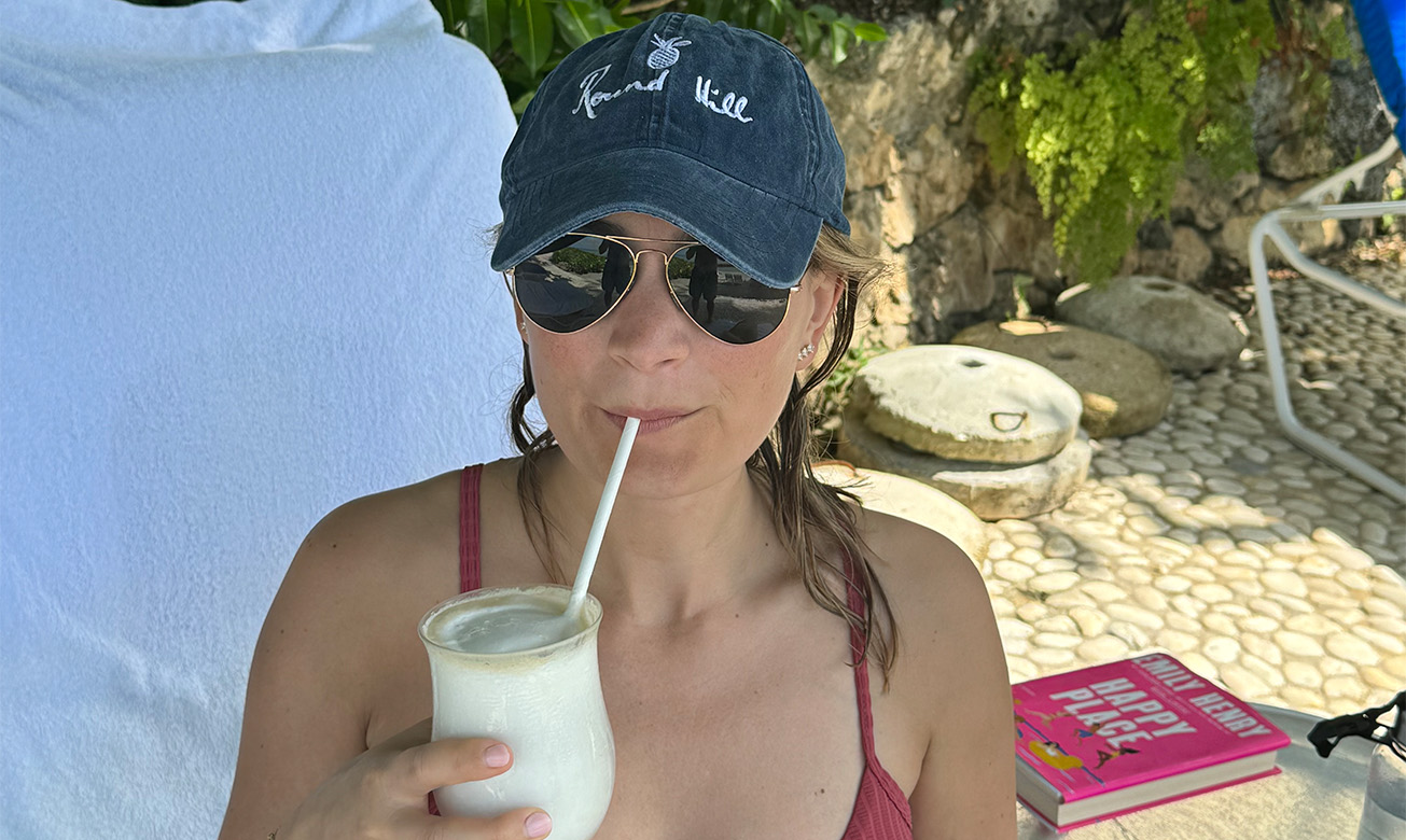 a woman wearing a hat and sunglasses drinking from a straw