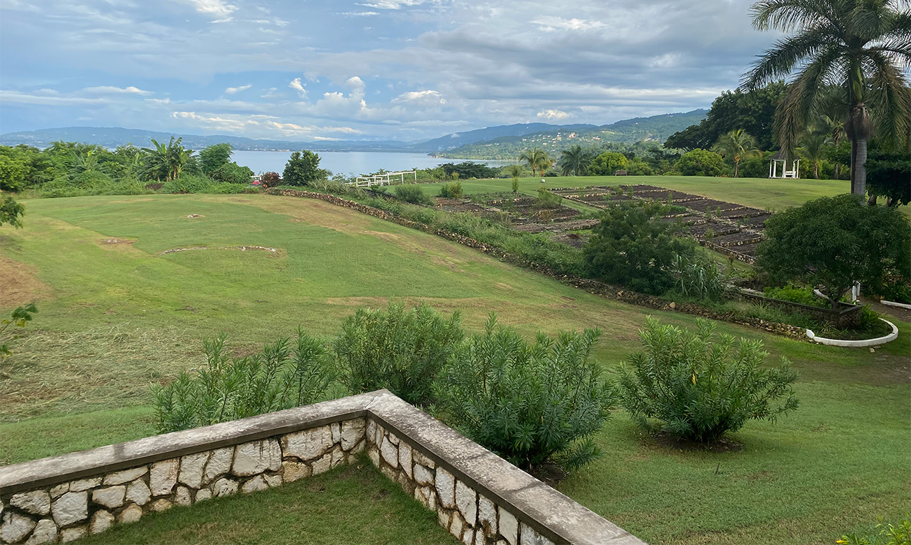 a landscape with a stone wall and a large field with trees and a body of water