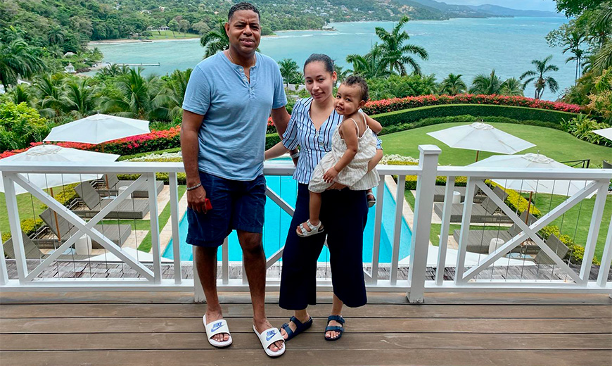 a man and woman standing on a deck with a baby and a pool in the background