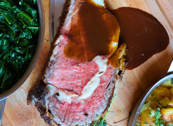 a piece of meat with sauce and vegetables on a cutting board