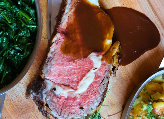 a piece of meat with sauce and vegetables on a cutting board