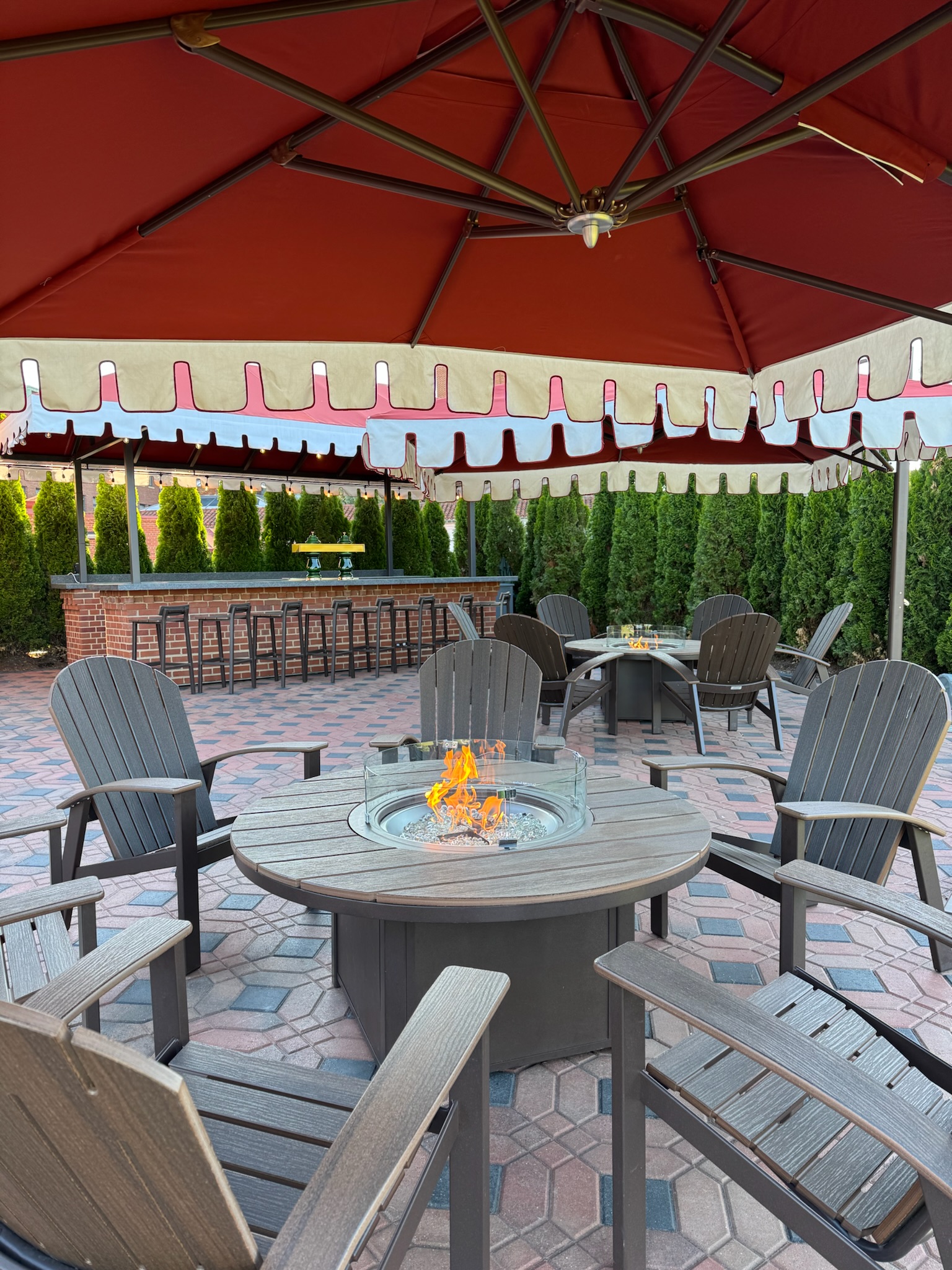 a patio with a fire pit and chairs under a red umbrella