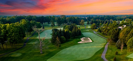a golf course with trees and a sunset
