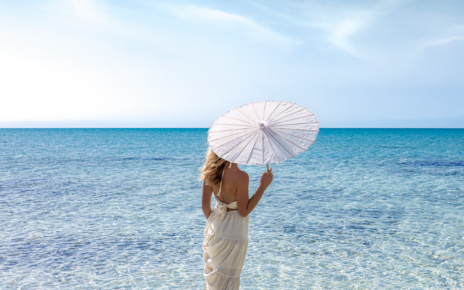 a woman in a white dress holding an umbrella in the water