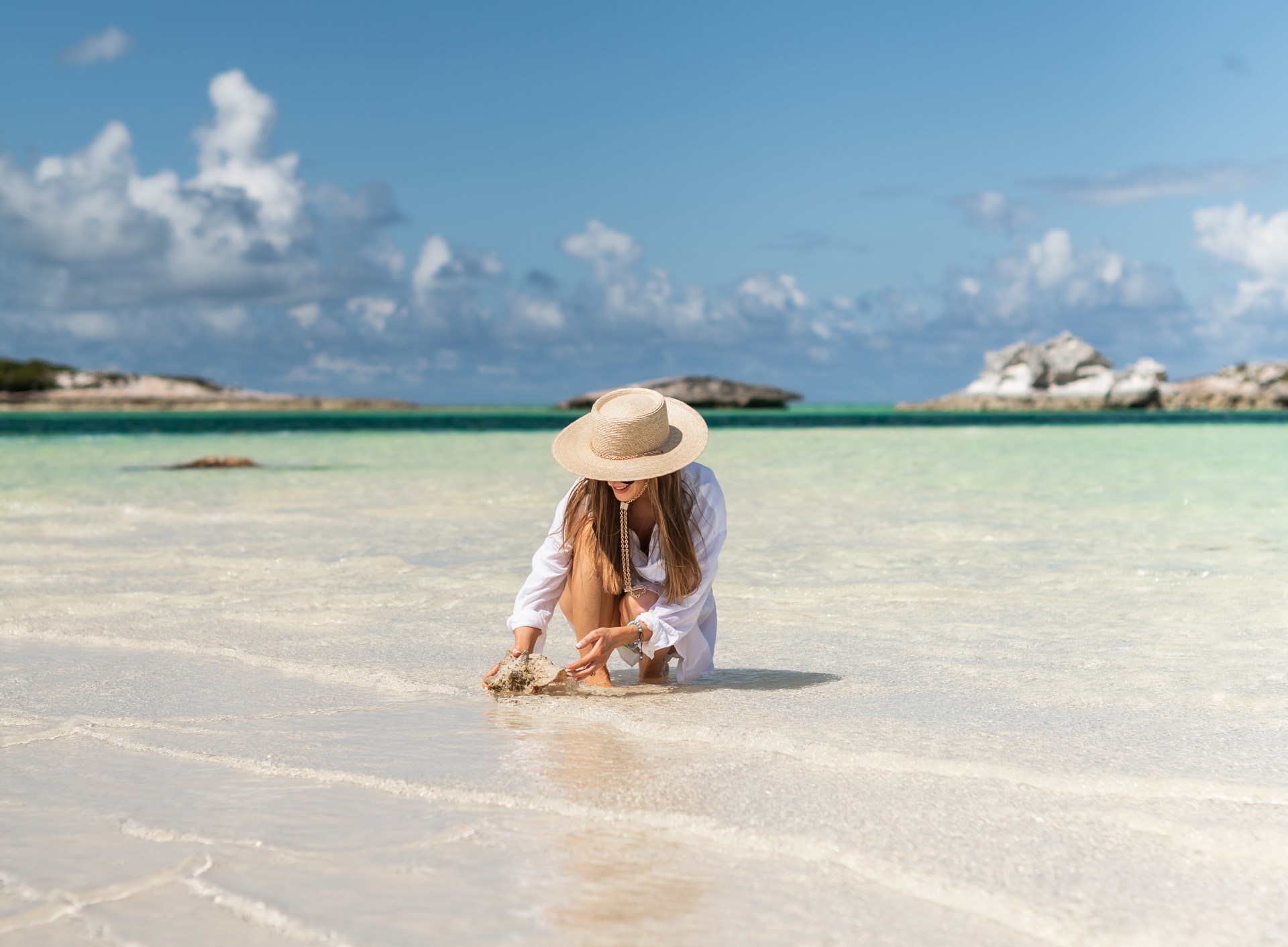 a woman in a hat playing with sand on a beach