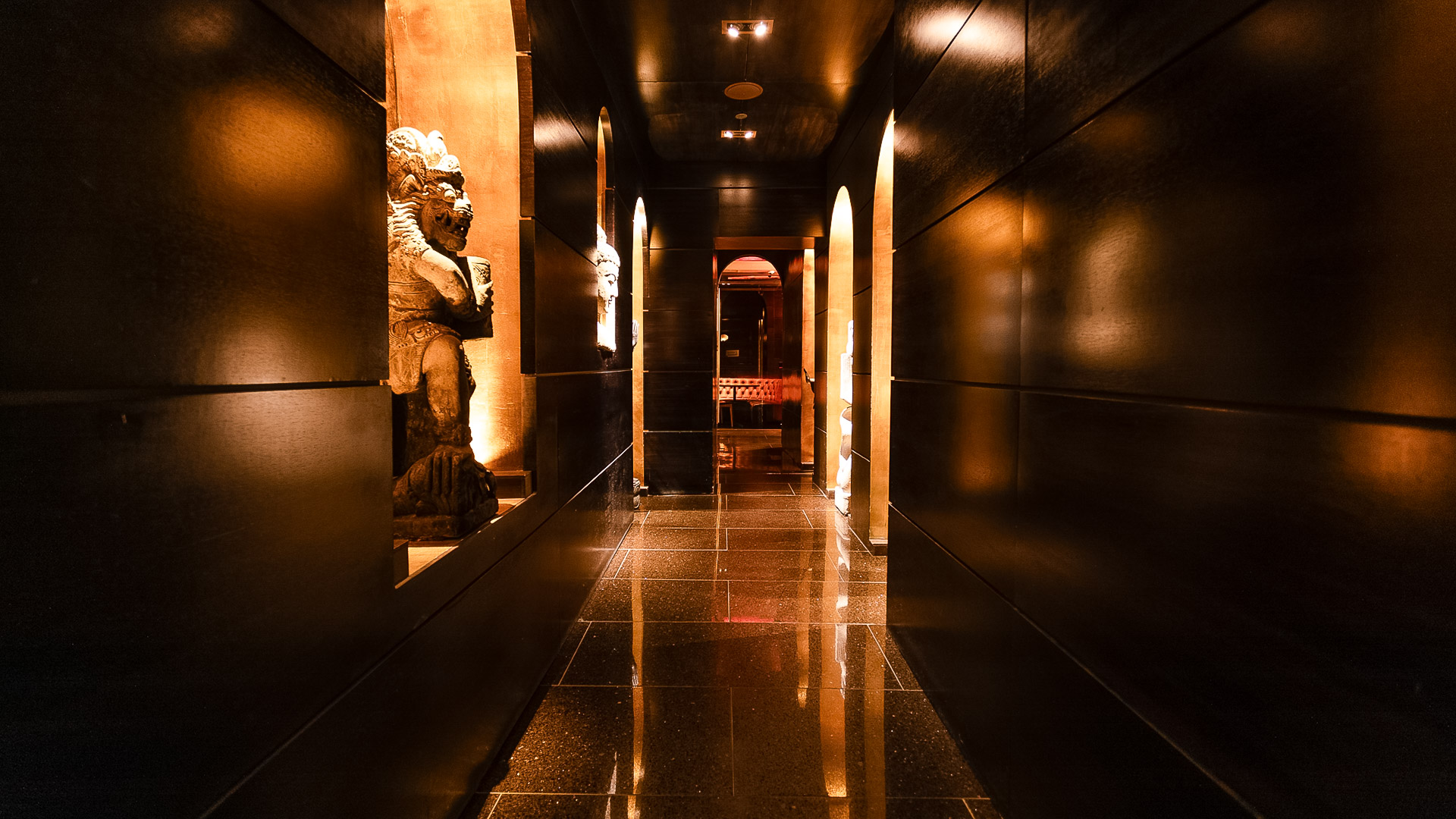 A dark hallway with a shiny floor and statues