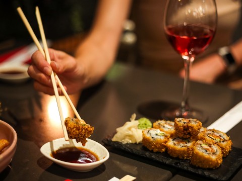 a person holding chopsticks over sushi