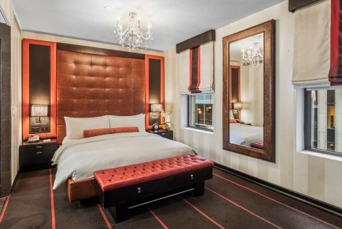 A wide view of a luxurious guest room with a large bed, tufted headboard and bench, chandelier, and mirror.