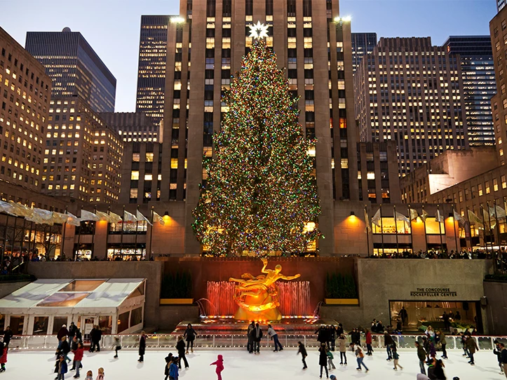a large tree with lights and people skating on ice
