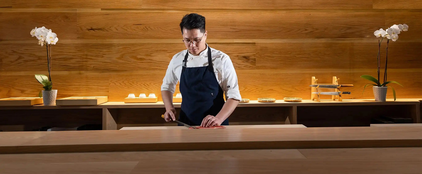 a man in a black apron cutting a piece of wood