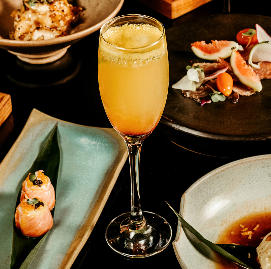 a glass of orange liquid next to plates of food