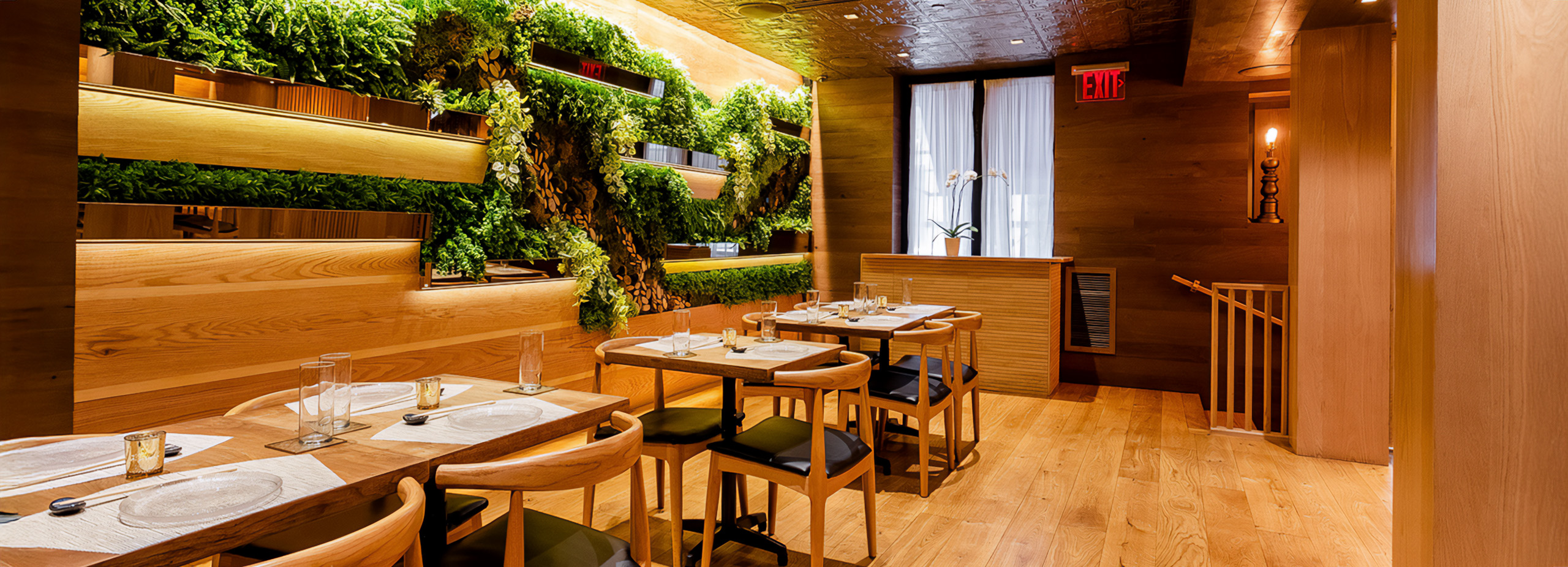 A dining area with wooden tables and chairs, a green wall, and light wood flooring.